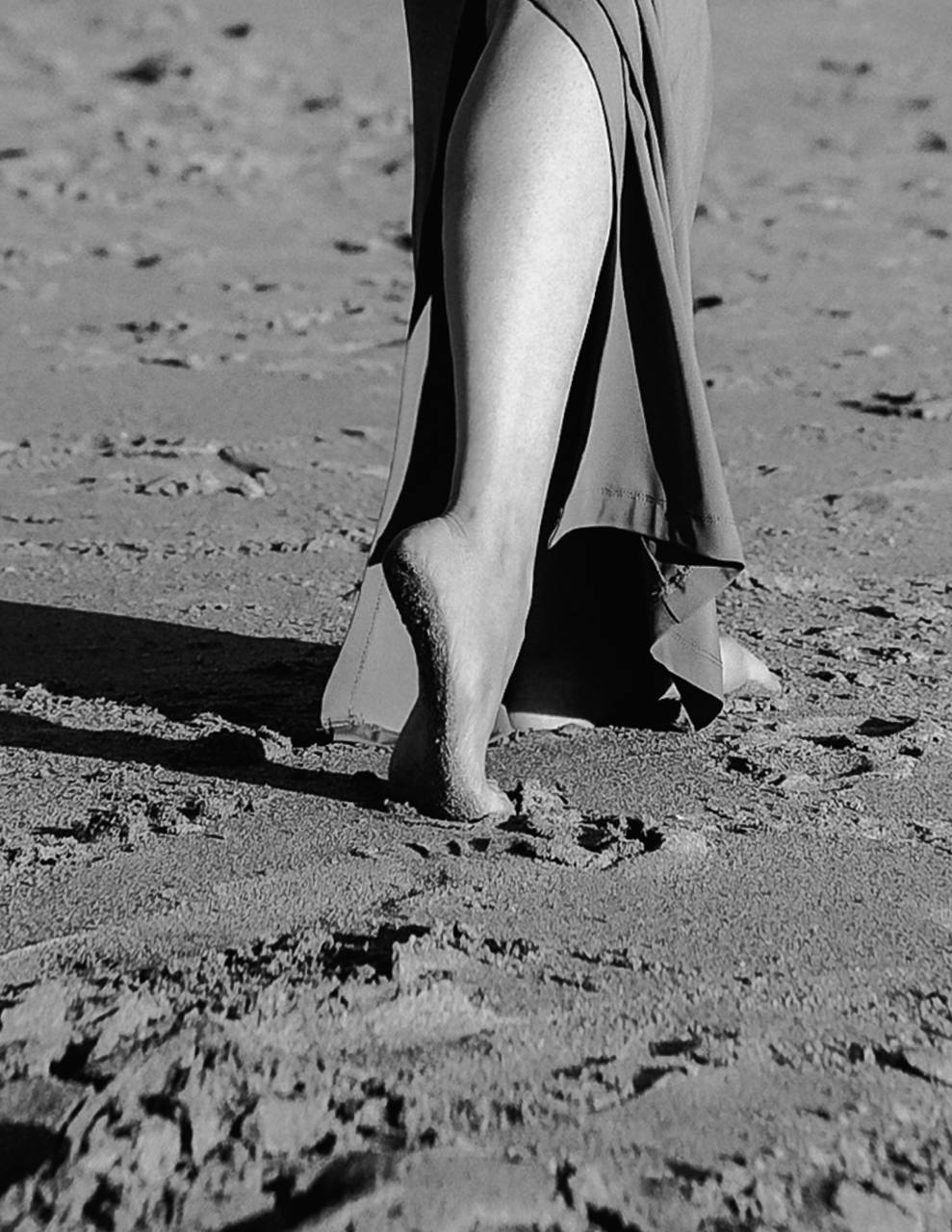 Woman's legs walking barefoot on sand.