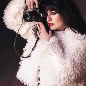Woman taking a photo wearing a faux white jacket.