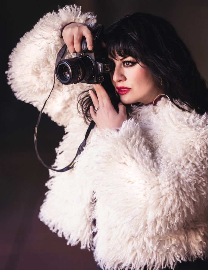 Woman taking a photo wearing a faux white jacket.